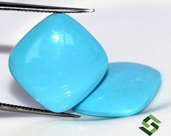 May include: Two polished, light blue gemstones with a square cushion cut. The gems are held by tweezers, showcasing their smooth, reflective surfaces. The background is white, highlighting the vibrant color of the stones.