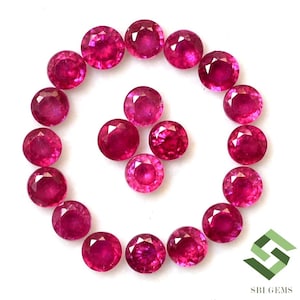 May include: A collection of 18 round, red ruby gemstones arranged in a circle on a white background.