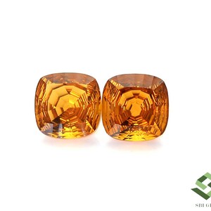 May include: Two cushion-cut, golden-yellow gemstones are displayed against a white background. The gems have a faceted surface that reflects light, creating a brilliant sparkle. The gems are a vibrant, warm color.