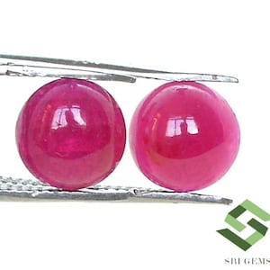 Peut inclure: Deux cabochons ronds en rubis rose, chacun d'environ 10 mm de diamètre, sont tenus par une pince argentée.