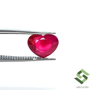 Può includere: Una pietra preziosa di rubino a forma di cuore, tenuta da una pinza, di colore rosso intenso.