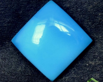 May include: A bright blue, diamond-shaped cabochon gemstone. The stone is smooth and polished, with a glossy finish.