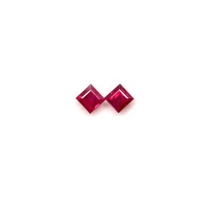 May include: Two square-cut, vibrant red gemstones are displayed against a stark white background. The gems are positioned side-by-side, showcasing their facets and intense colour. These gemstones are likely rubies, perfect for jewellery making.