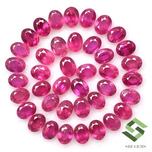 May include: A collection of 30 oval-shaped, pink ruby gemstones. The gemstones are arranged in a circle on a white background.