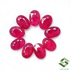 May include: Eight oval-cut rubies, each with internal facets, are arranged in a circle. The gemstones are a deep red hue, set against a white backdrop. The image highlights the clarity and sparkle of the stones. The rubies are likely to be measured in carats.