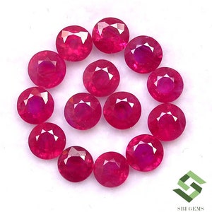 Puede incluir: Una colección de 14 piedras preciosas de rubí redondas y facetadas. Los rubíes son de color rojo intenso y están dispuestos en círculo.