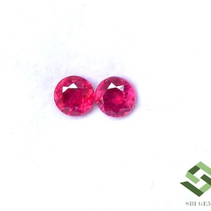 May include: Two round, faceted, bright red gemstones. The gems are set against a white background. The gems have a high degree of clarity and brilliance, reflecting light. The gems are likely rubies, suitable for jewelry making.