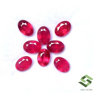 Puede incluir: Un conjunto de gemas rojas ovaladas, posiblemente rubíes, sobre un fondo blanco. Cada gema presenta una superficie facetada que refleja la luz. Ideal para joyería o coleccionistas de piedras preciosas.