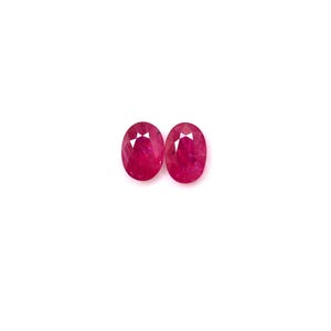 Puede incluir: Dos piedras preciosas de rubí de forma ovalada, cada una de color rojo intenso y talla facetada.
