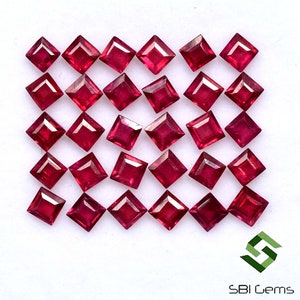 Puede incluir: Una colección de 25 piedras preciosas de rubí rojo sueltas, cada una cortada en forma cuadrada. Las piedras preciosas están dispuestas en filas sobre un fondo blanco.