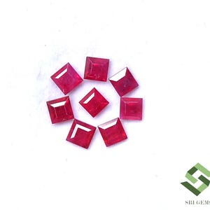 Peut inclure: Sept rubis rouges vifs de taille carrée sont disposés en cercle avec une pierre placée au centre. Chaque pierre précieuse présente des surfaces à facettes qui reflètent la lumière, mettant en valeur une teinte cramoisie profonde et une forme carrée uniforme.