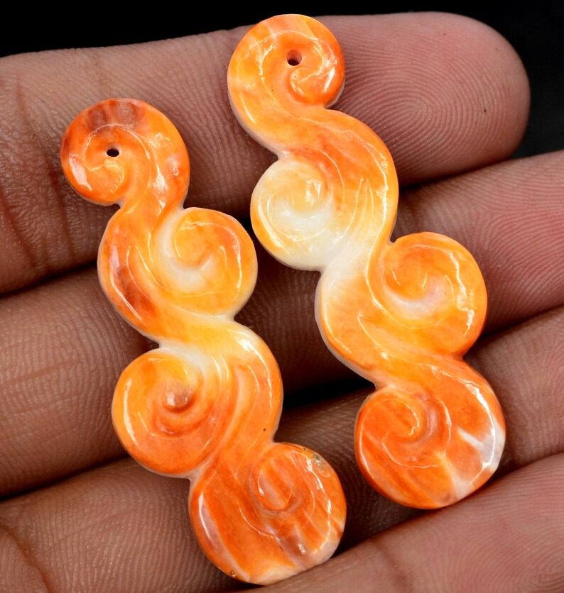 May include: Two orange and white carved shell pendants in the shape of swirling clouds. The pendants have a hole at the top for stringing.