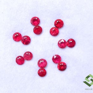 Puede incluir: Un conjunto de doce rubíes rojos pequeños, redondos y facetados dispuestos en un patrón circular. Cada piedra preciosa presenta un corte brillante con múltiples facetas triangulares que reflejan la luz, mostrando un color rojo intenso.