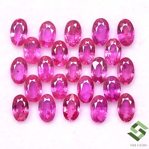 May include: A collection of 20 oval-shaped pink gemstones. The gemstones are arranged in a random pattern on a white surface.
