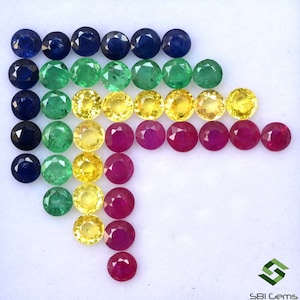 May include: Assortment of round gemstones in various colors, including blue sapphires, green emeralds, yellow sapphires, and red rubies. The gemstones are arranged in rows, with the largest stones at the top and the smallest stones at the bottom.