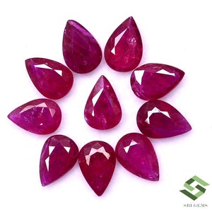 May include: Ten pear-shaped ruby gemstones, each with a deep red hue and a faceted cut. The gemstones are arranged in a circular pattern on a white background.