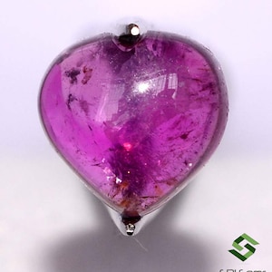 May include: A heart-shaped, pink gemstone cabochon with a silver setting. The gemstone has a translucent appearance with visible inclusions.