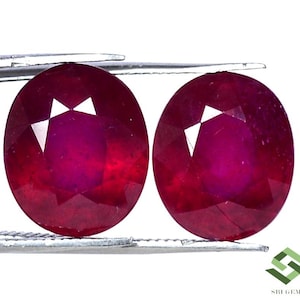 Puede incluir: Dos piedras preciosas redondas de rubí rojo con un corte facetado. Los rubíes están engastados en un engaste plateado.