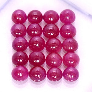 Pode incluir: Uma coleção de 18 cabochões de rubi de forma oval, cada um com uma superfície lisa e polida e uma cor vermelha profunda e rica.