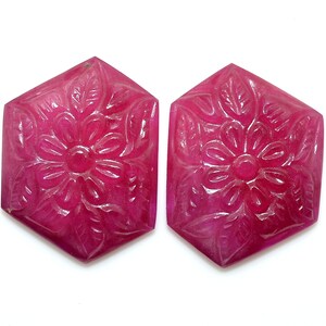 Pode incluir: Duas pedras preciosas de rubi rosa esculpidas com um design floral. As pedras preciosas são de forma hexagonal e têm um acabamento polido.