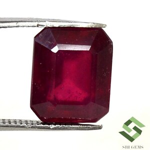May include: A deep red emerald cut gemstone, held in a metal clamp.