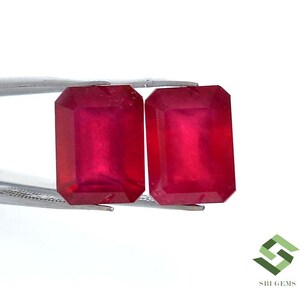 Puede incluir: Dos piedras preciosas de color rojo vibrante talladas en esmeralda, sostenidas por pinzas. Las piedras preciosas son lisas y pulidas, mostrando su brillo.