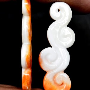 May include: A white and orange carved shell pendant in the shape of a cloud. The pendant has a hole at the top for hanging.