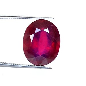 Peut inclure: Une pierre précieuse ovale de couleur rouge foncé avec une taille facetée. La pierre précieuse est tenue par une pince.