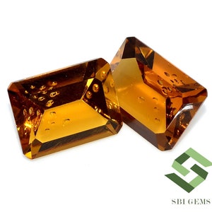 May include: Two rectangular, faceted gemstones with a warm, amber hue. The gems have a slight internal texture and are set against a white background. The gems are likely for jewelry making or collecting.