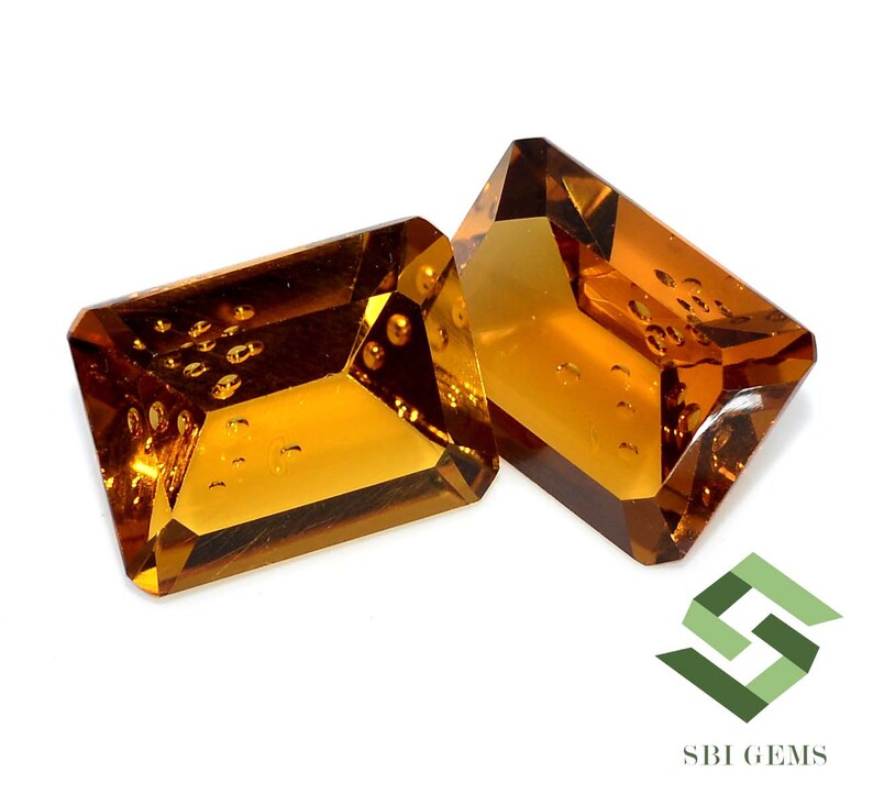 May include: Two rectangular, faceted gemstones with a warm, amber hue. The gems have a slight internal texture and are set against a white background. The gems are likely for jewelry making or collecting.