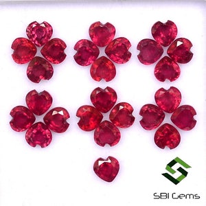 Könnte beinhalten: Eine Sammlung von 13 herzförmigen Rubin-Edelsteinen, wobei 12 in drei Gruppen zu vieren angeordnet sind und ein einziger herzförmiger Rubin-Edelstein darunter liegt. Die Edelsteine sind tiefrot und haben eine polierte Oberfläche. Das Bild enthält auch den Text "SBI Gems".