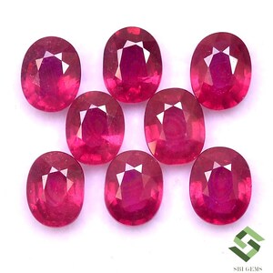 Puede incluir: Ocho piedras preciosas de rubí de forma ovalada, cada una con un color rojo intenso y un corte facetado. Las piedras preciosas están dispuestas en un grupo suelto sobre un fondo blanco.