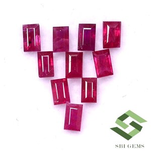 May include: A collection of ten faceted ruby gemstones in a rectangular shape. The gemstones are arranged in a triangular pattern on a white background.