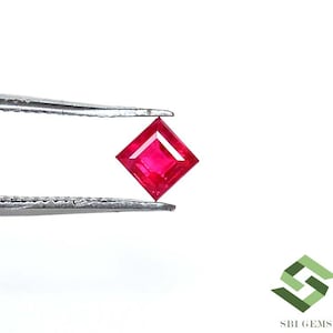 May include: A vibrant, square-cut ruby gemstone held by tweezers. The gemstone is a deep, rich red color, with a symmetrical shape and facets that catch the light. The tweezers are silver-colored.