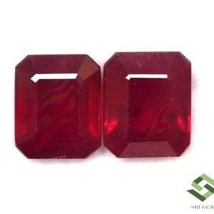 May include: Two radiant-cut, deep red gemstones are displayed against a white background. The gems have a rectangular shape with beveled edges and a bright, reflective surface. The gems are likely rubies, and are ideal for jewelry making.