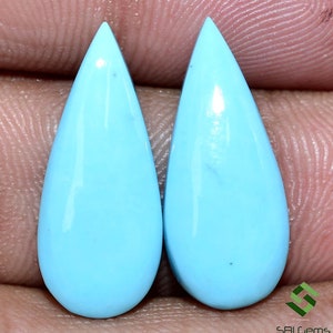 May include: Pair of teardrop shaped turquoise cabochons. The stones are a light blue color and have a smooth, polished finish.