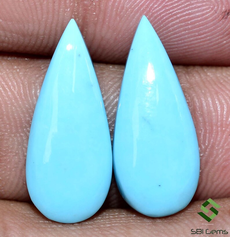 May include: Pair of teardrop shaped turquoise cabochons. The stones are a light blue color and have a smooth, polished finish.