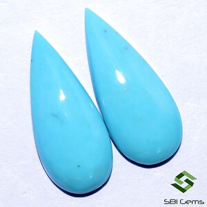 May include: Two teardrop-shaped turquoise cabochons, each with a smooth, polished surface and a light blue color.