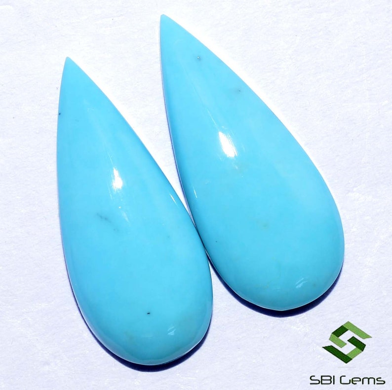 May include: Two teardrop-shaped turquoise cabochons, each with a smooth, polished surface and a light blue color.