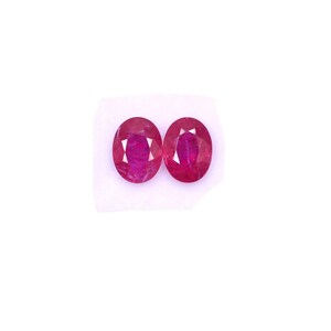 May include: Two oval-shaped ruby gemstones, each with a deep red color and a faceted cut.