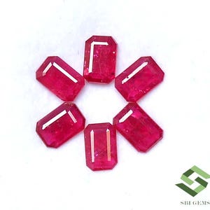May include: Six rectangular-cut ruby gemstones, arranged in a circular pattern. Each gem has a deep red colour and a polished surface. The gems are set against a white background, enhancing their colour and clarity. The gems are approximately 1 cm in length.