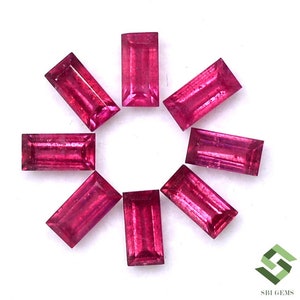 May include: Eight red ruby gemstones in a baguette cut. The gemstones are arranged in a circle on a white background.