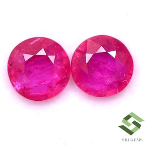 May include: Two round, faceted, pink ruby gemstones. The gemstones are approximately the same size and shape.
