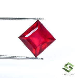 May include: A vibrant red square-shaped gemstone held by tweezers. The gemstone is cut with facets and has a polished finish.