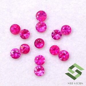 Puede incluir: Una colección de doce piedras preciosas redondas de color rosa. Las piedras preciosas están dispuestas en forma de estrella sobre una superficie blanca.