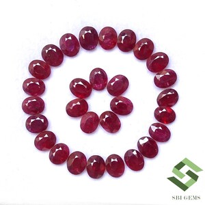 May include: Oval-cut rubies arranged in a spiral pattern on a white background. The gemstones are a deep red color and have a faceted surface, reflecting light. The image includes the SBI GEMS logo in the bottom right corner.