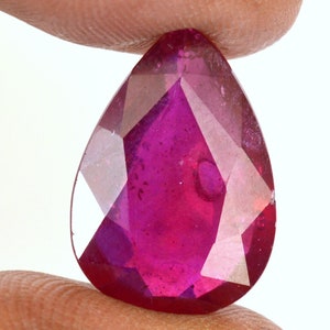 Puede incluir: Una piedra preciosa de rubí en forma de pera, de color rojo intenso y tallada a facetas.