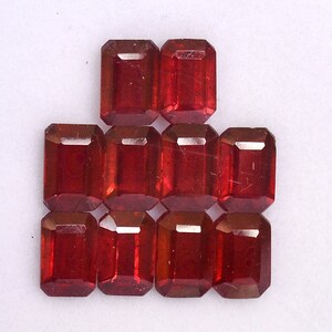 May include: Ten red gemstone cabochons in an emerald cut. The gemstones are arranged in a pyramid shape.