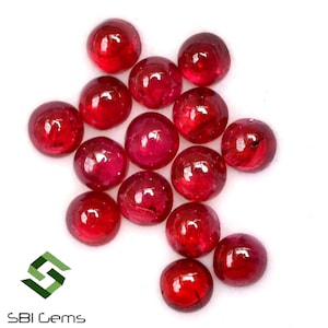 Pode incluir: Um grupo de 16 cabochões redondos de rubi vermelho, cada um com uma superfície lisa e polida. As pedras estão dispostas em um aglomerado solto, com algumas sobreposições.