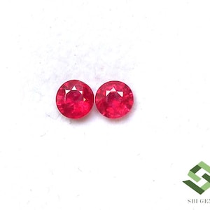 May include: Two round, faceted, bright red gemstones. The gems are set against a white background. The facets create a starburst effect in the center of each gem. The gems are likely rubies.